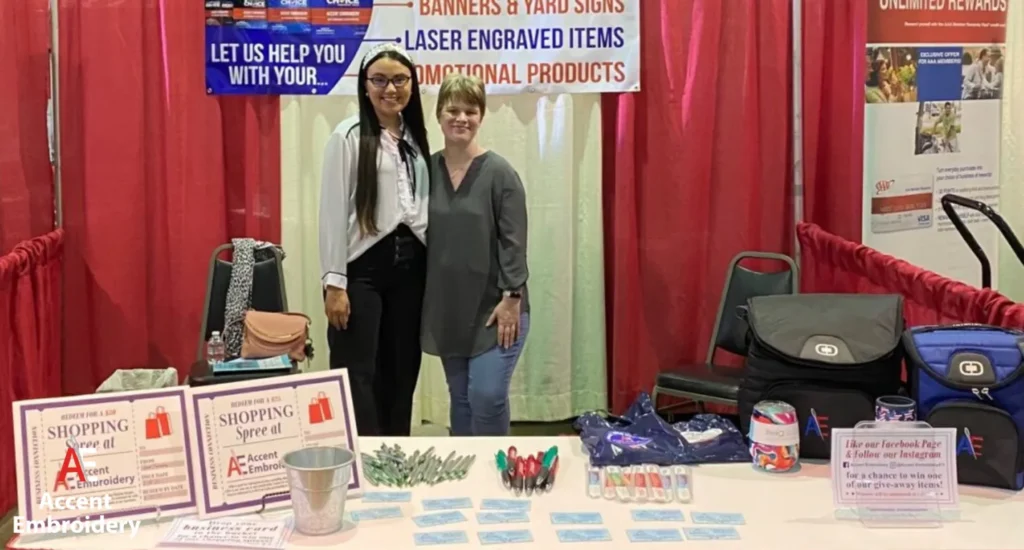Two women are positioned by a table highlighting laser engraving options at Accent embroidery Two women are positioned by a table highlighting laser engraving options at Accent embroidery